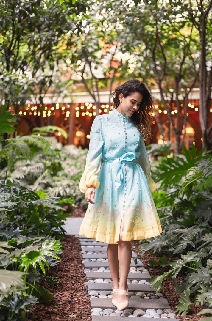 Vestido corto con efecto ombré, manga larga abullonada, botones joya al frente y aplicaciones brillantes. Disponible en rosa/naranja y verde/azul. El look perfecto para brillar este verano.