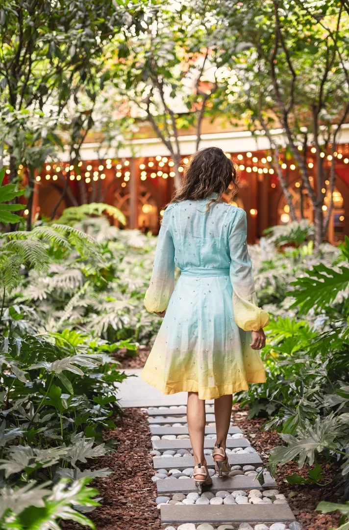 Vestido corto con efecto ombré, manga larga abullonada, botones joya al frente y aplicaciones brillantes. Disponible en rosa/naranja y verde/azul. El look perfecto para brillar este verano.