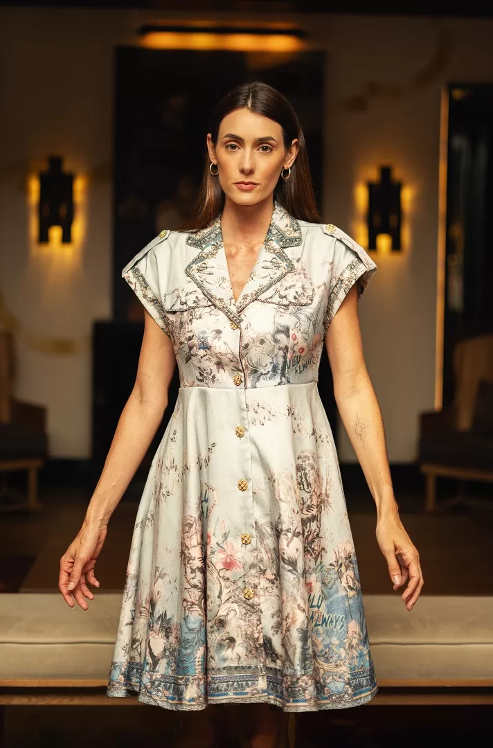 Vestido camisero con print artístico estilo toile de Jouy en tonos suaves, cuello estructurado, hombreras con botón dorado y pedrería en solapas. Elegancia atemporal con espíritu moderno.