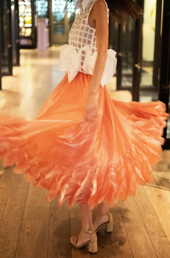 Falda midi rosa con olanes asimétricos y caída fluida en textil satinado. Una pieza statement con movimiento espectacular y elegancia única.